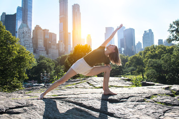 Flexible woman doing yoga pose in city park in New York at sunset time