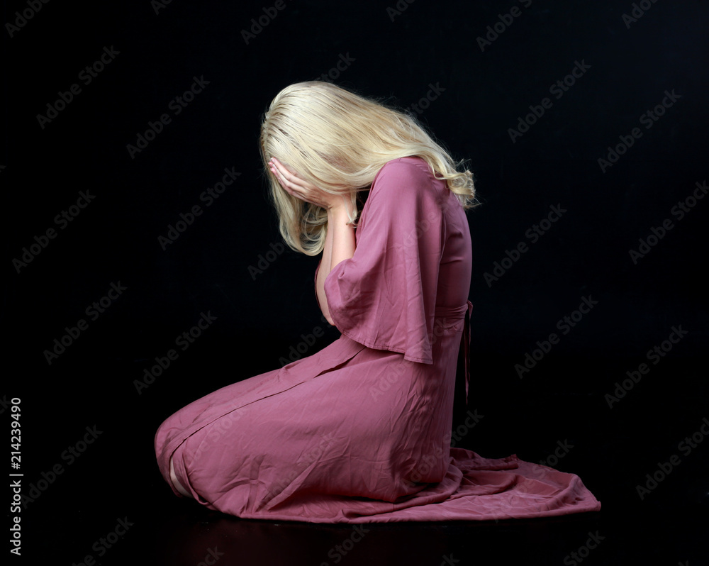 Poster full length portrait of blonde girl wearing long purple dress. seated pose. black studio background.