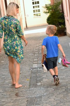 young woman in a dress is walking with a little boy down the street