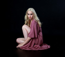 full length portrait of blonde girl wearing long purple dress. seated pose. black studio background.