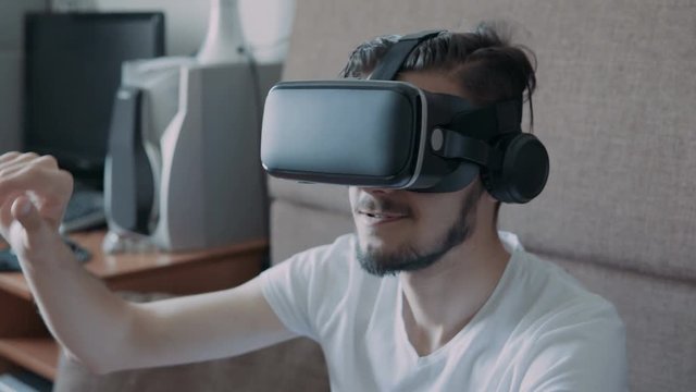 Close up shot of a young bearded man wearing virtual reality glasses - surfing net via virtual reality interface.