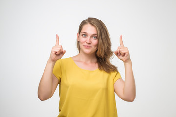 Smiling european woman in yellow shirt pointing finger up.