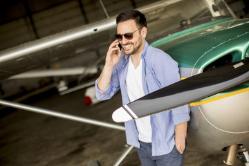 Handsome young pilot checking airplane in the hangar and using mobile phone © BGStock72