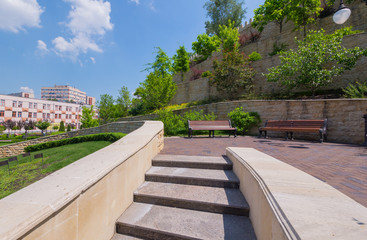 Steps leading to a small square with long benches and a wall with green spaces in several levels