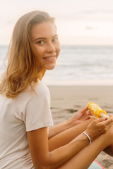 Healthy diet. Vegetarian hipster girl eat fresh organic grilled corn and look to camera. Sporty lady on sea beach sunset or ocean sunrise. Travel, active, yoga, vegan and dieting lifestyle concept.