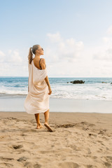 Pretty girl in casual clothes and wooden sunglasses stay on the hot sand. Beautiful lady on sea exotic beach sunset or ocean sunrise. Travel, explore, active yoga and meditation lifestyle concept.