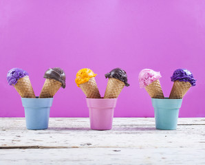 Various ice-cream scoops on fuchsia background with assorted balls of blueberry, chocolate, strawberry and orange icecream in waffles
