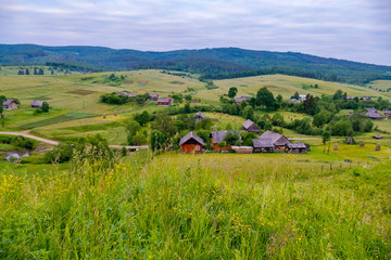 Naklejka premium A charming landscape of mountainous terrain with rural houses located on the slopes and valley between green trees.