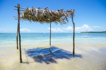 Rustic palm frond and tree branch palapa stands waiting to shade visitors to the shallow waters on a remote tropical beach in northeastern Bahia, Brazil