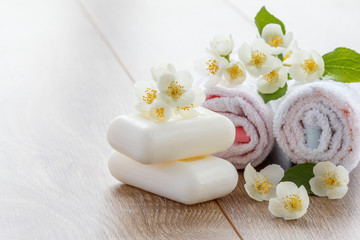 Obraz na płótnie Canvas White towels and soap for bathroom procedures and flowers of jasmine on wooden boards