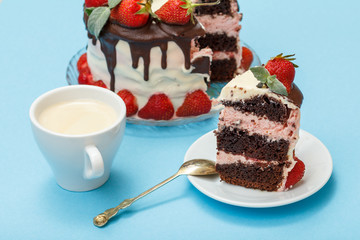 Cup of coffee, piece of cake with spoon on white saucer and homemade chocolate cake decorated with fresh strawberries on glass plate