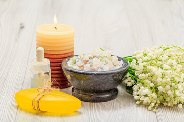 Obraz na płótnie Canvas Soap, bottle with aromatic oil, burning candle, bowl with sea salt and bouquet of lilies of the valley