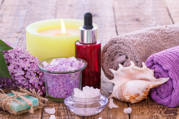 Obraz na płótnie Canvas Lilac flowers, soap, burning candle, bowls with sea salt, red bottle with aromatic oil, sea shell and towels