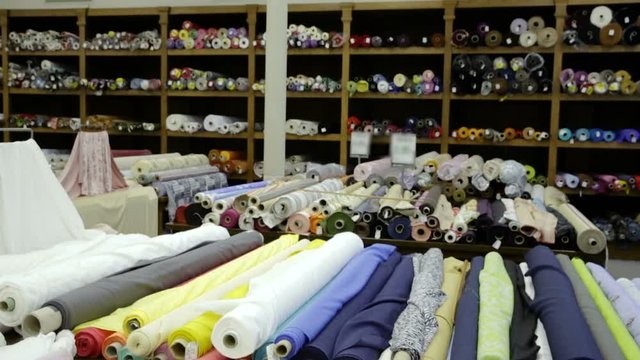 Rolls of fabric and textiles for sale stacked on shelves in shop