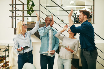 Ecstatic group of diverse businesspeople high fiving in an offic