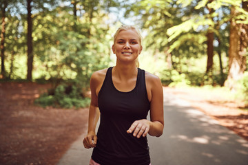 Smiling young blonde woman jogging alone along a forest path