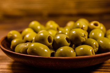 Ceramic plate with green olives on wooden table