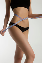 The beautiful thin woman measures waist number in black lingerie by the blue measuring device. Narrow waist, thin long legs. Sport, diets, loss of weight.