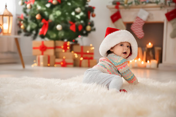 Obraz na płótnie Canvas Cute little baby in Santa hat sitting on fur rug at home. Christmas celebration