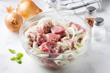 Marinated raw pork meat with onions, herbs and spices for cooking skewers, barbecue. In glass bowl on light background
