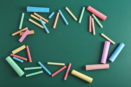 Color pieces of chalk on green background, top view