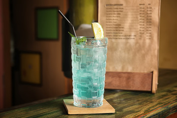Glass with delicious cocktail and ice cubes on counter in bar