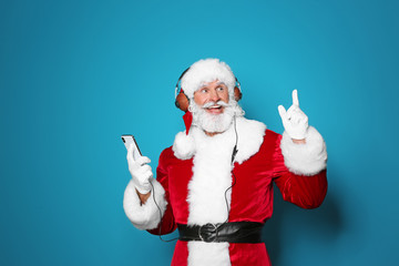 Santa Claus listening to Christmas music on color background