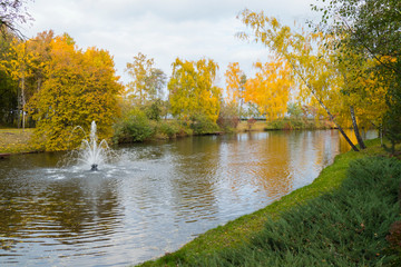 A small decorative fountain in the middle of a transparent lake against the backdrop of beautiful autumn trees