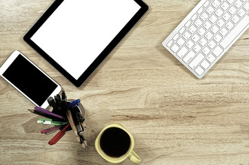 blank screen smartphones and tablet PC on the wooden desktop with computer keyboard and a cup of coffee in composition with copy space for your text