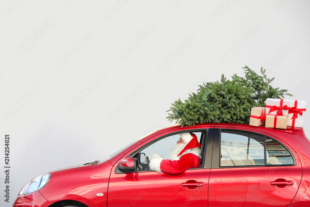 Wall mural Authentic Santa Claus driving red car with gift boxes and Christmas tree, view from outside