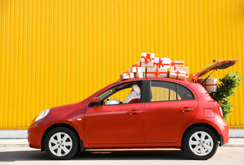 Authentic Santa Claus driving red car with gift boxes and Christmas tree, view from outside