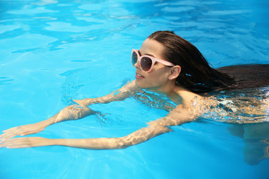 Beautiful young woman swimming in blue pool