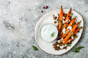 Roasted carrots lentil salad with feta, herb yogurt and dukkah on a light concrete background....