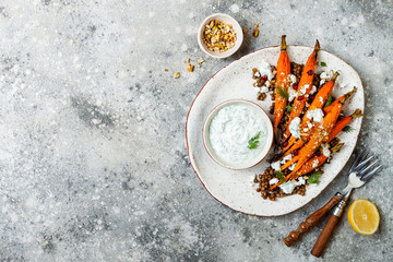 Roasted carrots lentil salad with feta, herb yogurt and dukkah on a light concrete background....