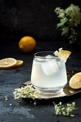 A glass of homemade elderflower gin sour or lemonade garnished with freshly picked elderflowers.