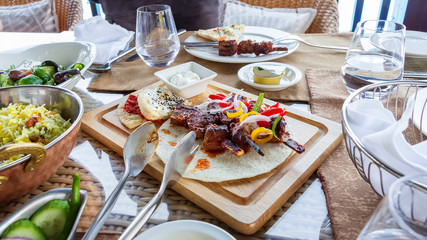 Barbecue grill meat served with vegetables, tortilla and sauce on wooden cutting board. Served table