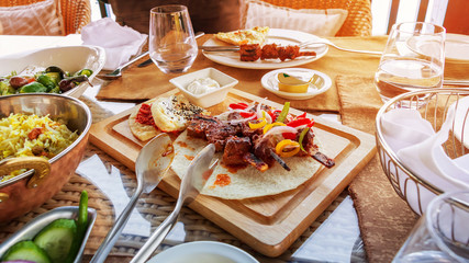 Barbecue grill meat served with vegetables tortilla and sauce on wooden cutting board. Served lunch.  Sunlight toned photo.