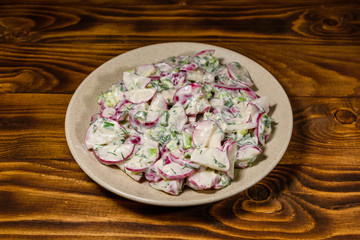 Vegetarian salad with radish, green onion and sour cream on a ceramic plate