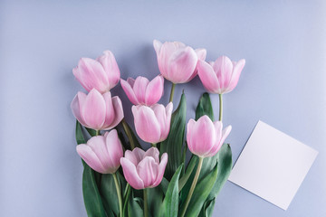 Pink tulips flowers and sheet of paper over light blue background. Greeting card or wedding invitation. Flat lay, top view