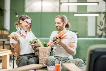 Young vegetarian couple sitting on the sofa with bag full of fresh vegetables in the beautiful green home interior
