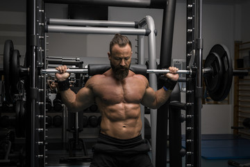 Hombre fuerte con grandes músculos haciendo sentadillas mientras entrena en el gimnasio. Ponerse en forma.