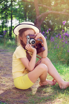Toned portrait of Cute little girl in retro outfit taking pictures with old film camera.