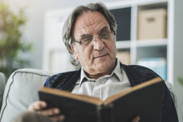 Old man reading book at home