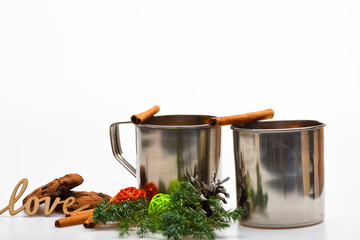 Mugs with mulled wine or hot drink near winter decoration and cookies on white background, close up. Hot wine concept. Mulled wine or hot beverage in metal mugs with cinnamon sticks and word love
