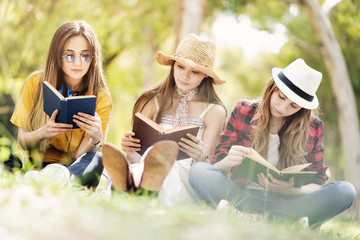 Young friends sitting and reading book on grass outside