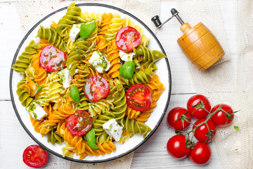 Italian food - Salad with colorful pasta, cherry tomatoes, feta cheese and fresh basil on white wooden background