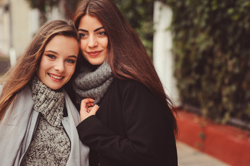 two young happy girlfriends walking on city streets in casual fashion outfits, wearing warm coats and having fun