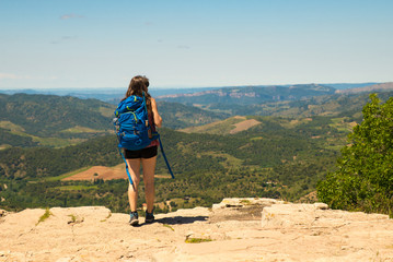 Naklejka premium Backpacker adventurer girl admiring the landscape from top of a cliff
