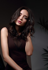 Fototapeta premium Beautiful makeup brunette model with curly hairstyle looking sexy on dark shadow background. Closeup portrait
