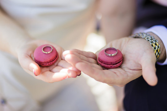 A wedding couple holds macaroons with the rings put on them. Wedding theme.